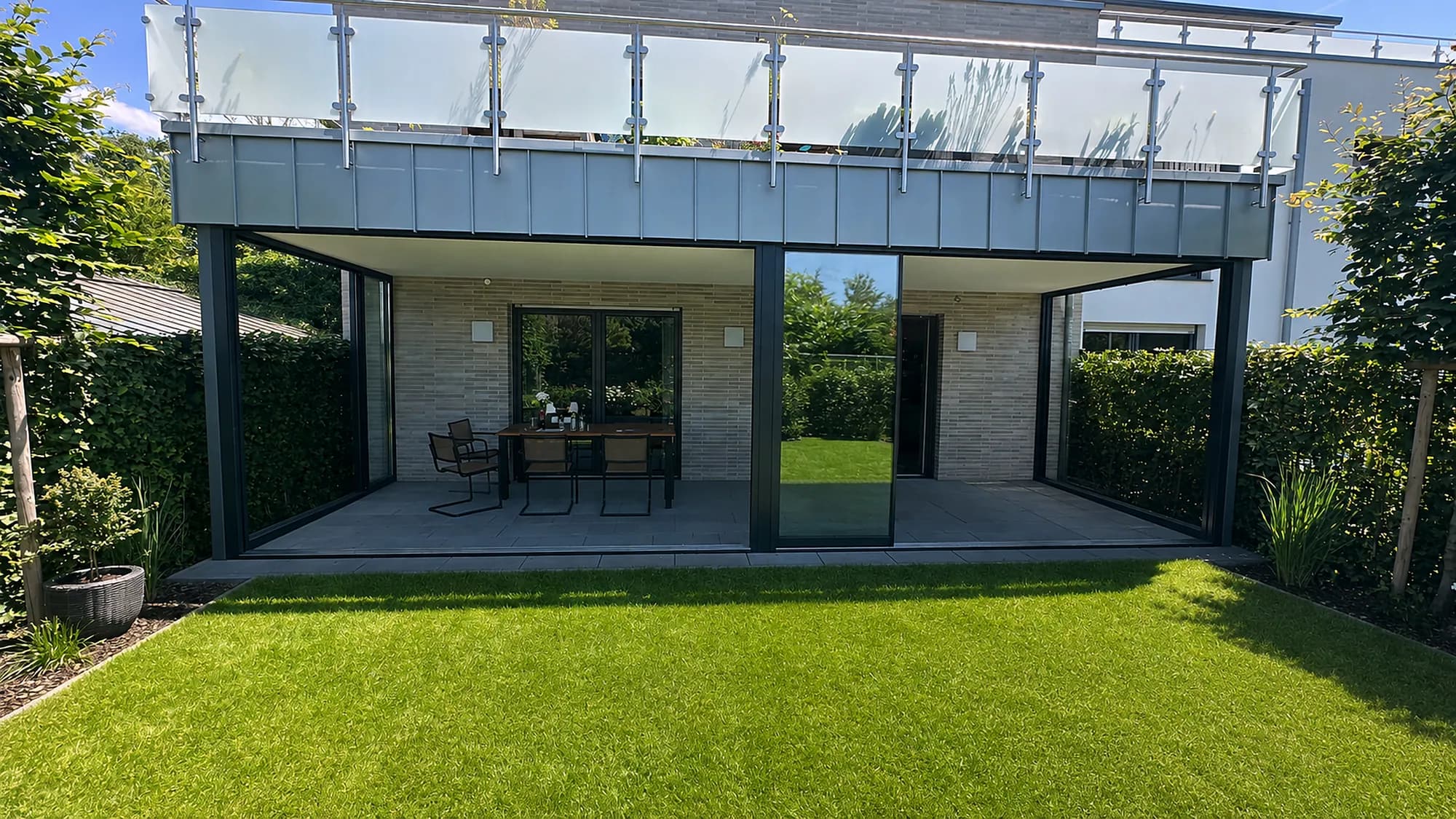 Terrasse mit Glasgeländer über einem überdachten Sitzplatz im Garten
