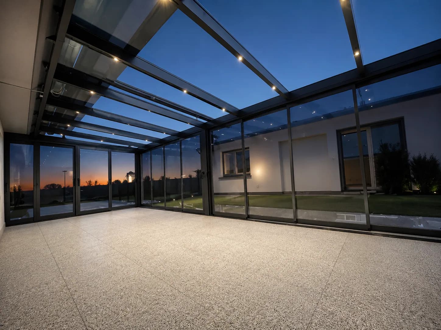 Glashaus in der Abenddämmerung mit LED-Spots im Glasdach und Steinteppichboden