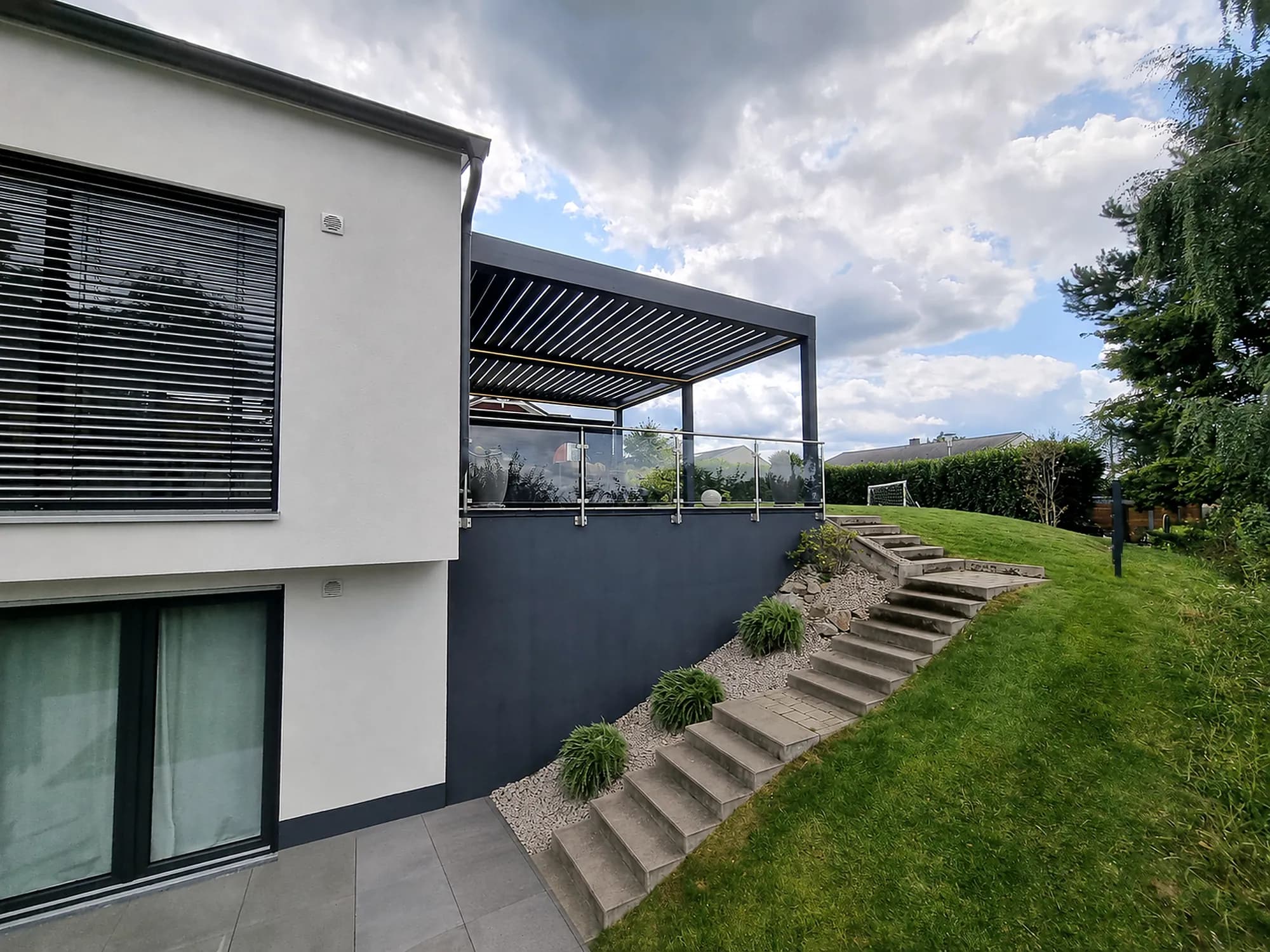 Lamellendach auf der Terrasse eines weißen Wohnhauses in Hanglage