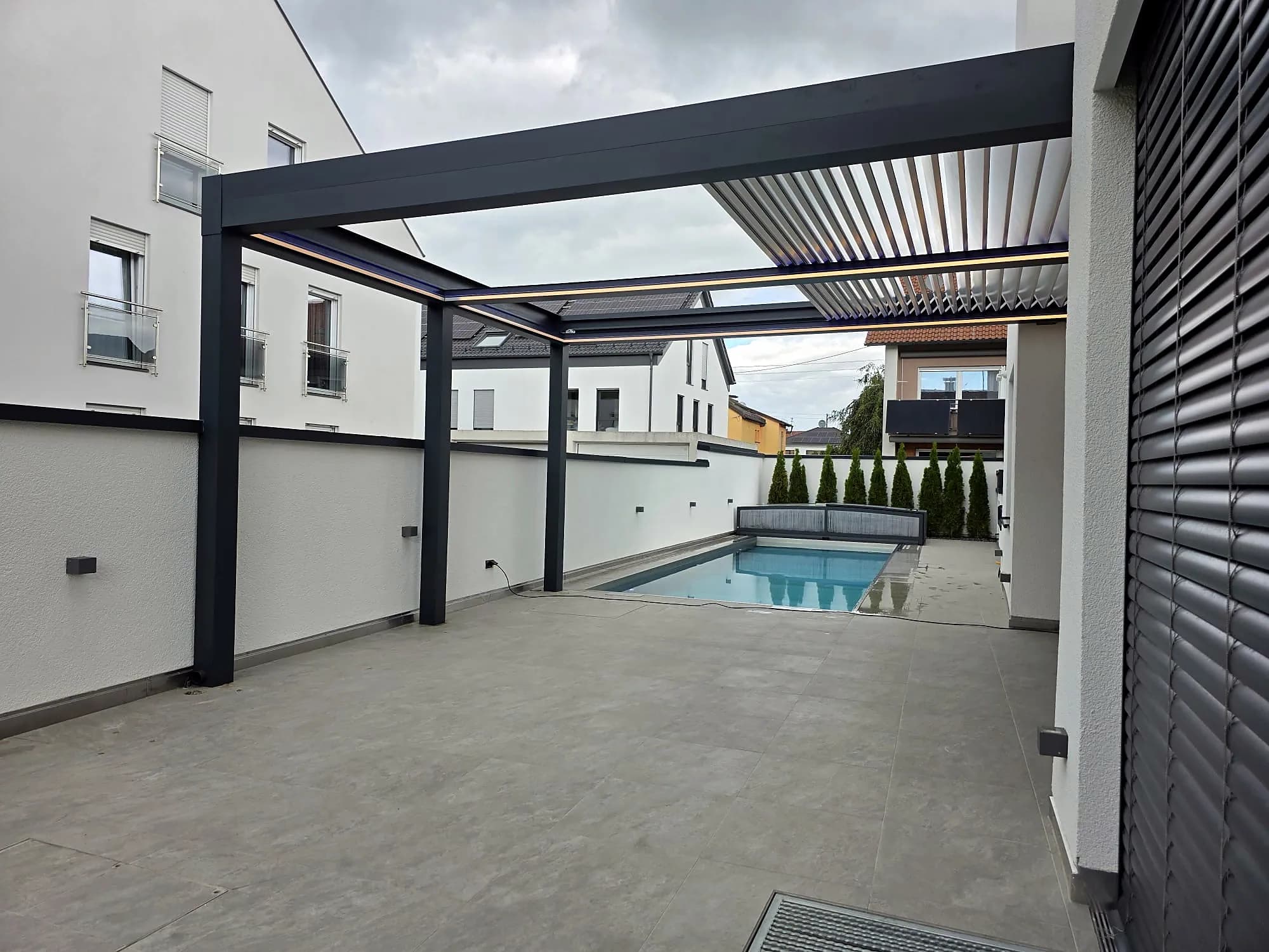Lamellendach über der Terrasse mit Blick auf Pool und Garten
