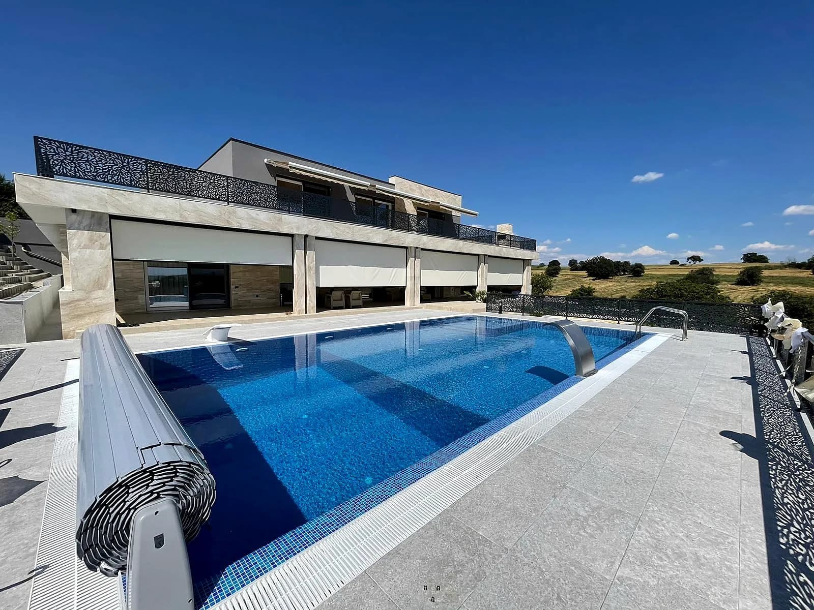 Pool mit elektrischer Rollabdeckung vor einem modernen Wohnhaus