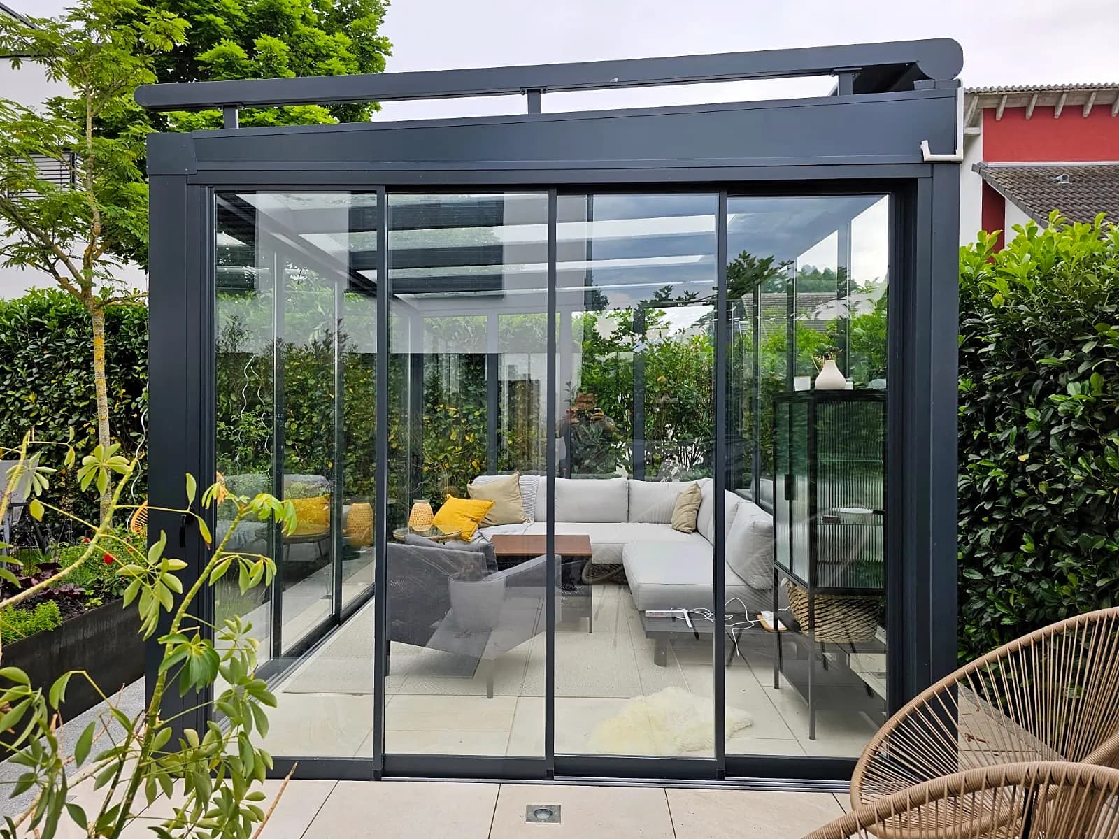 Glashaus mit Lounge, umgeben von Hecken und Pflanzkübeln