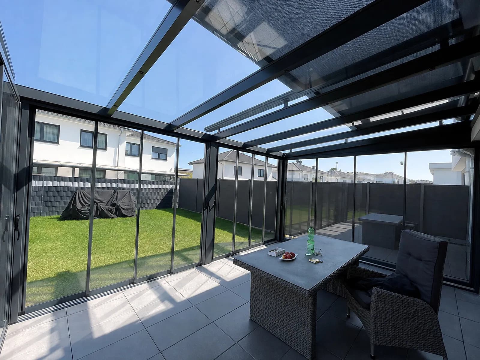 Glashaus innen mit Essplatz und geöffneten Schiebeelementen zum Garten