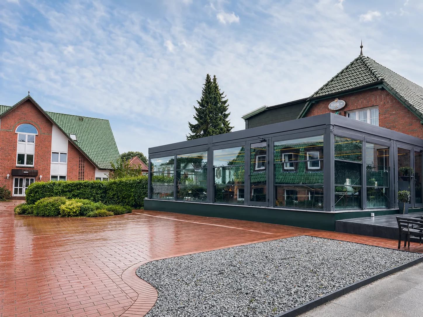 Glashaus an einem Klinkerhaus mit gepflasterter Einfahrt