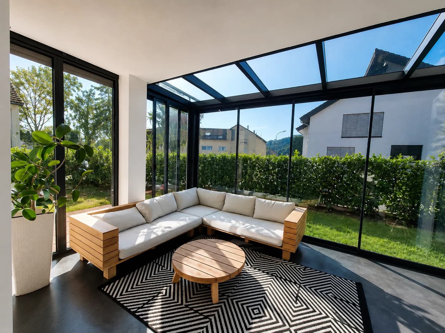Innenansicht eines Glashauses mit heller Lounge und Blick auf Rasen und Hecke