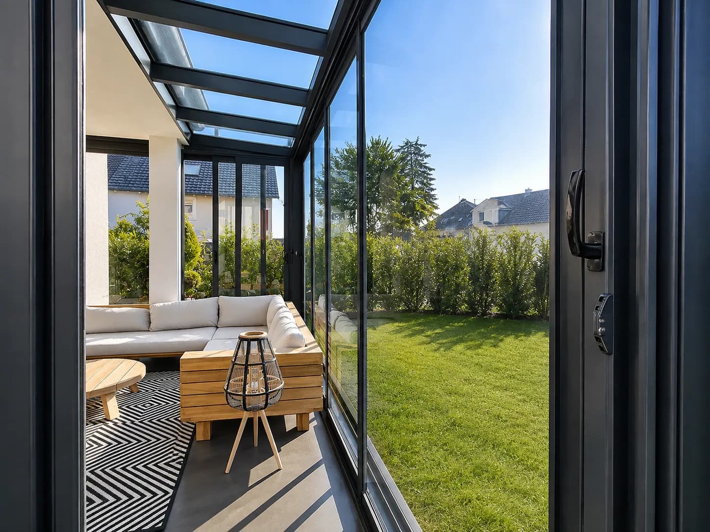 Sommergarten mit Loungemöbeln, offener Glasschiebewand und Blick in den Garten