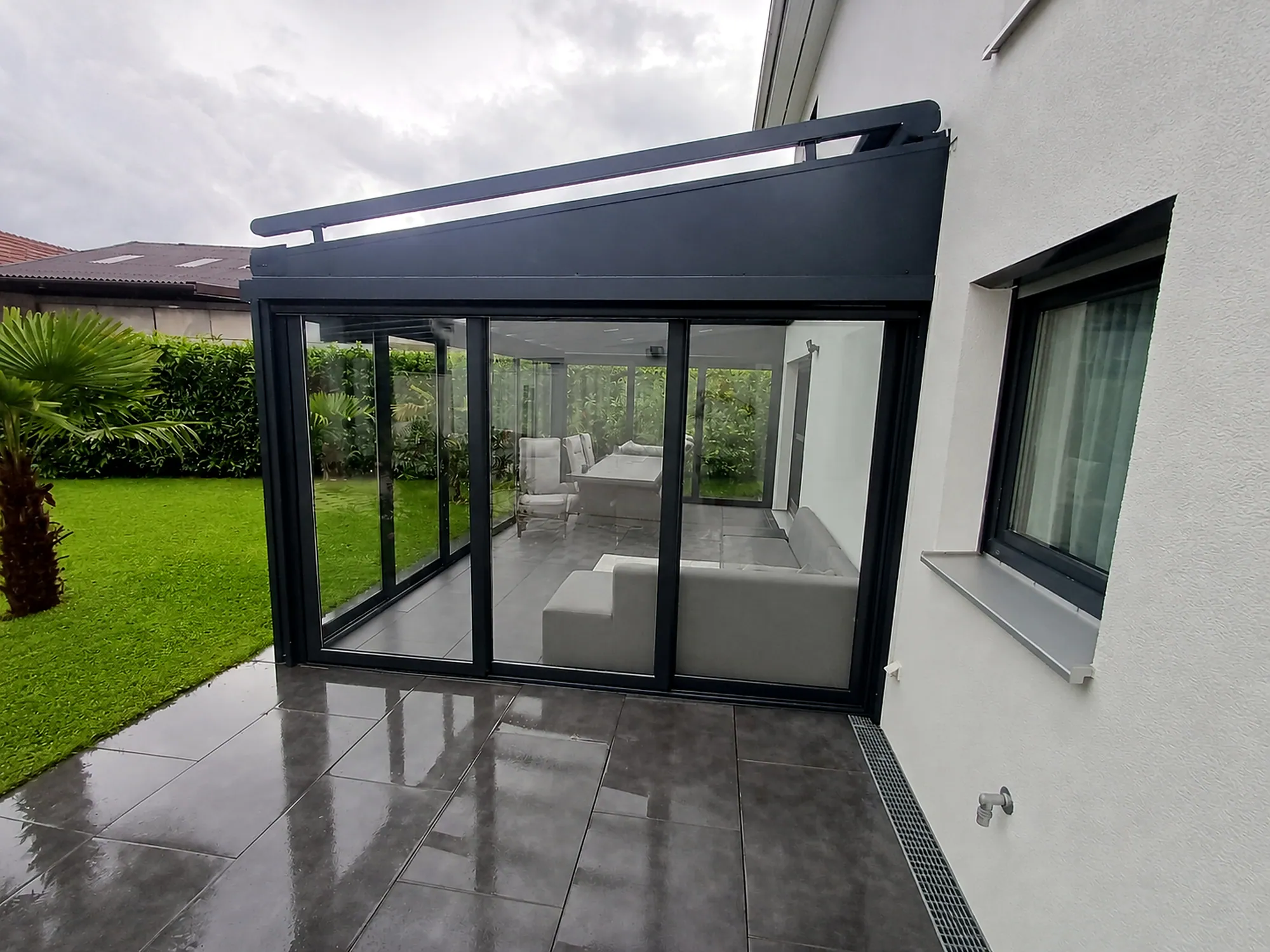 Glashaus mit heller Lounge an einem modernen Wohnhaus