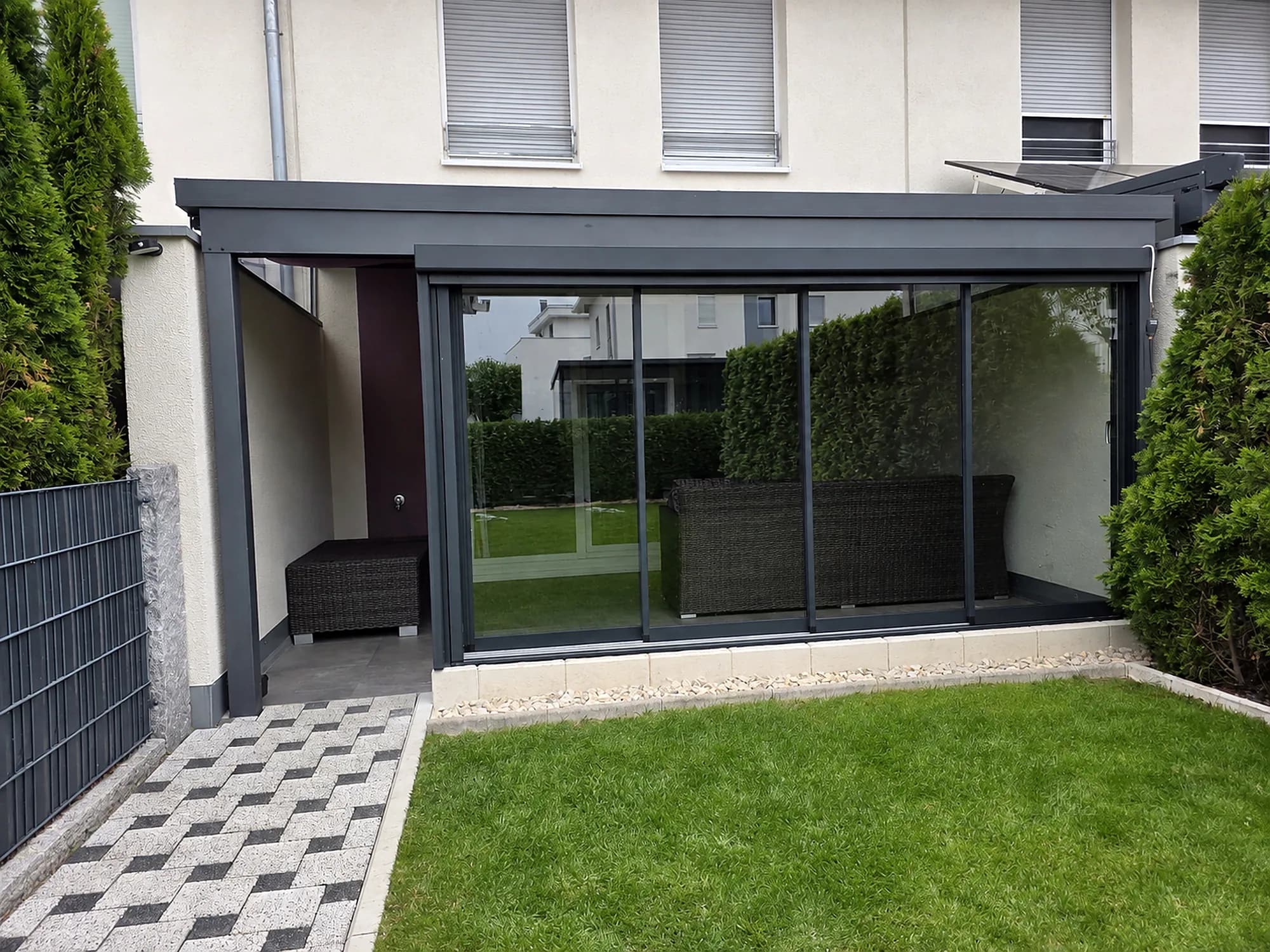 Glashaus mit Schiebeelementen an einem weißen Wohnhaus, Blick über den Rasen